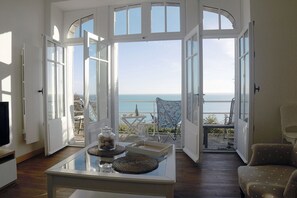 A spacious room with large windows offering a view of the sea. There is a glass table with decorative items and a chair.