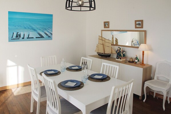 A dining area with a white table set for six, white chairs, a ship model, and a mirror above the table.