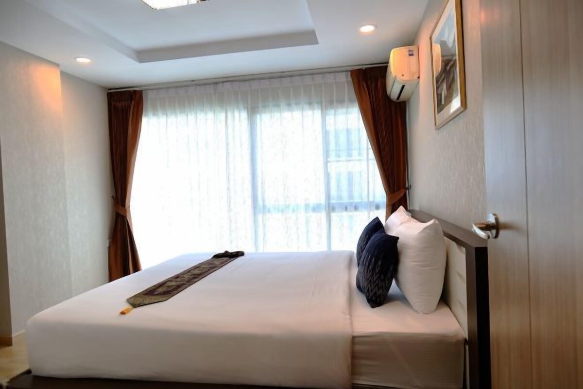 A hotel room with a large bed, curtains, a ceiling light, and a framed picture on the wall.