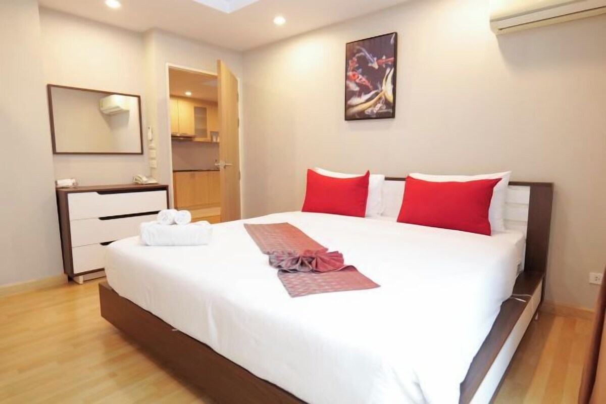A hotel room with a large bed, a bedside table, a mirror, and a painting on the wall.