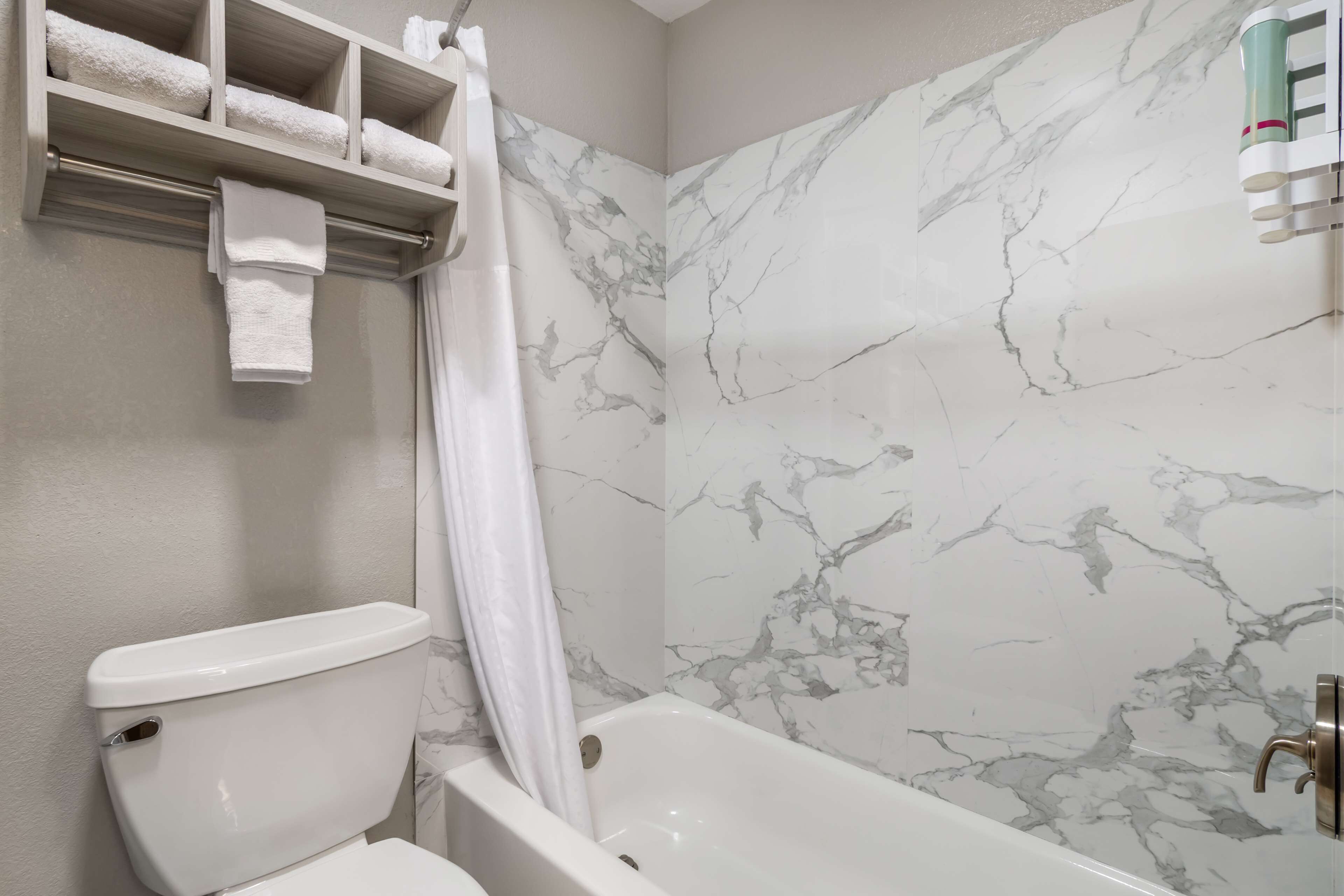 A bathroom with a toilet, a bathtub, and a marble wall.
