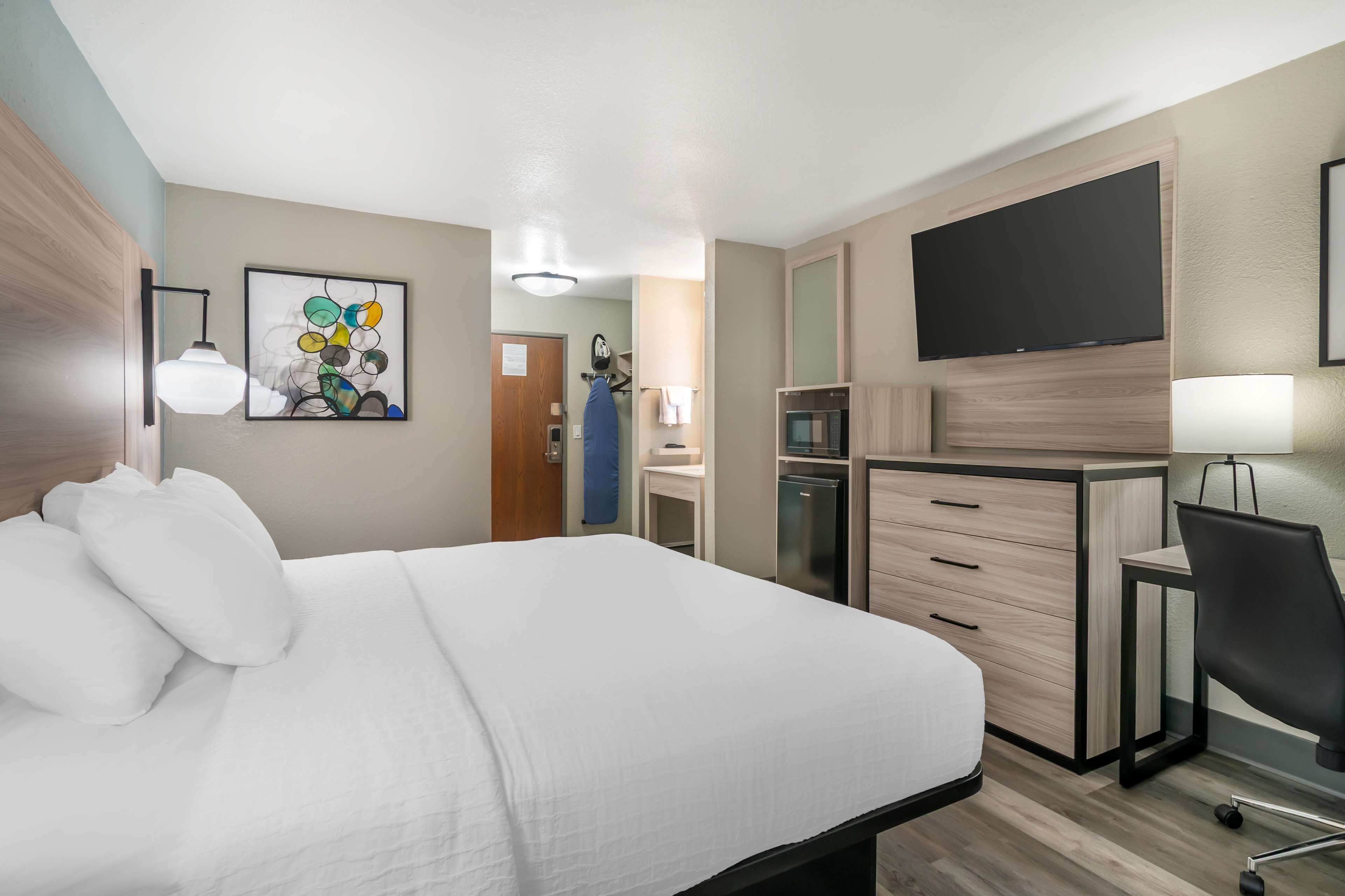 Camera d'albergo con letto, scrivania, sedia, televisore e angolo cottura.