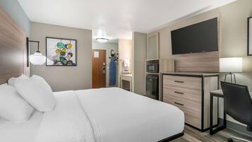 Camera d'albergo con letto, scrivania, sedia, televisore e angolo cottura.