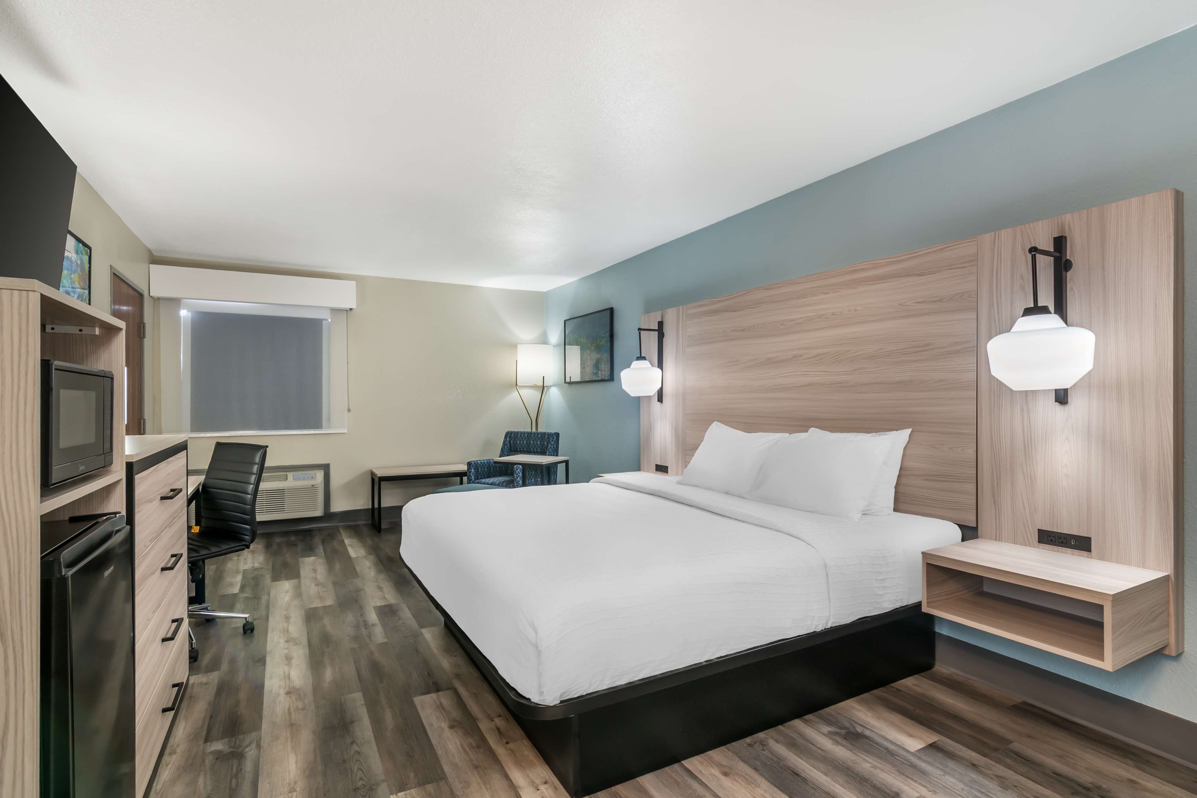 A modern hotel room with a bed, desk, chair, and built-in TV.