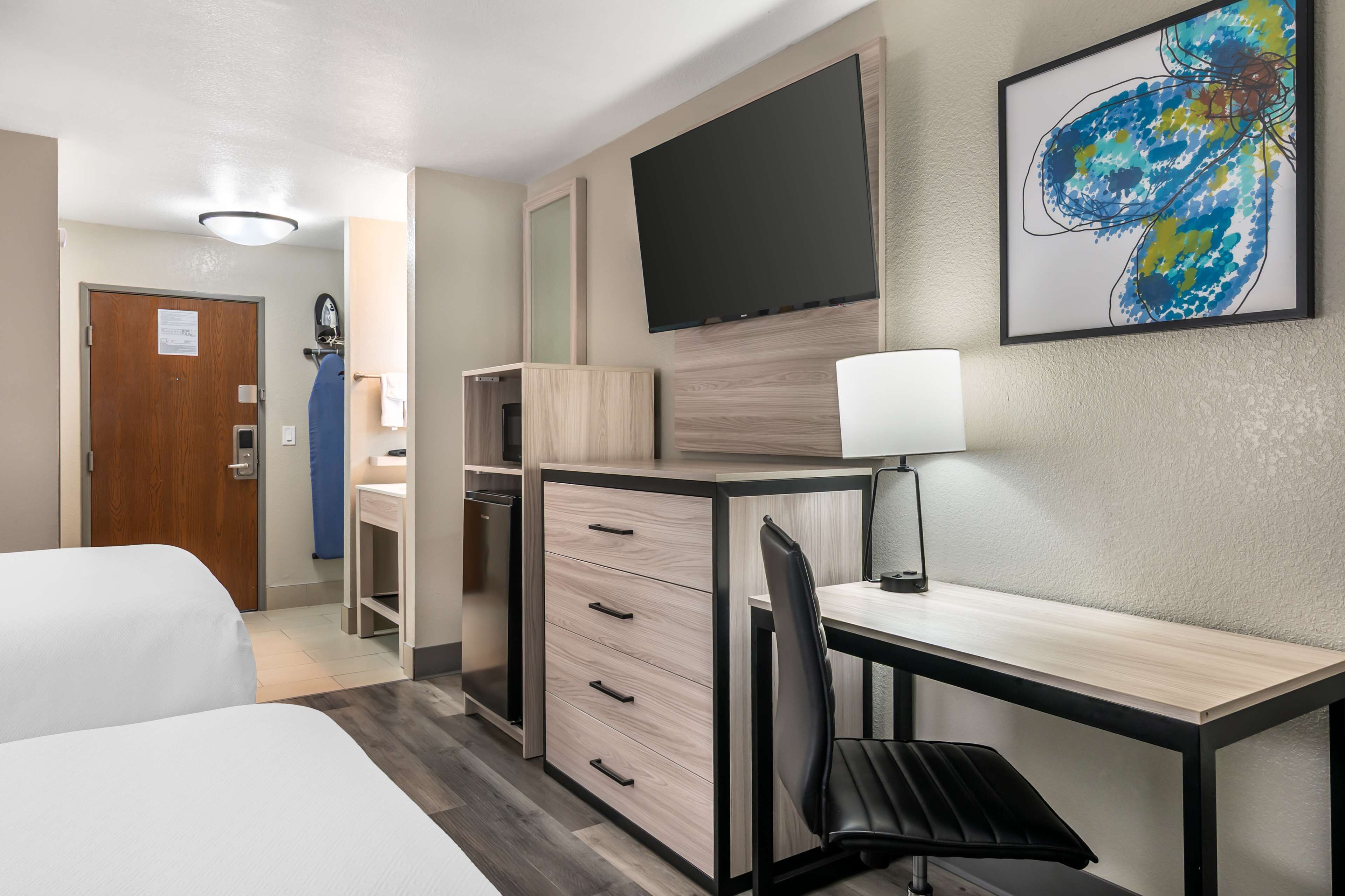 A hotel room with a bed, a desk, a chair, a TV, and a painting on the wall.