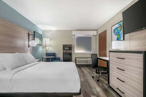 A hotel room with a bed, desk, chair, dresser, and artwork.