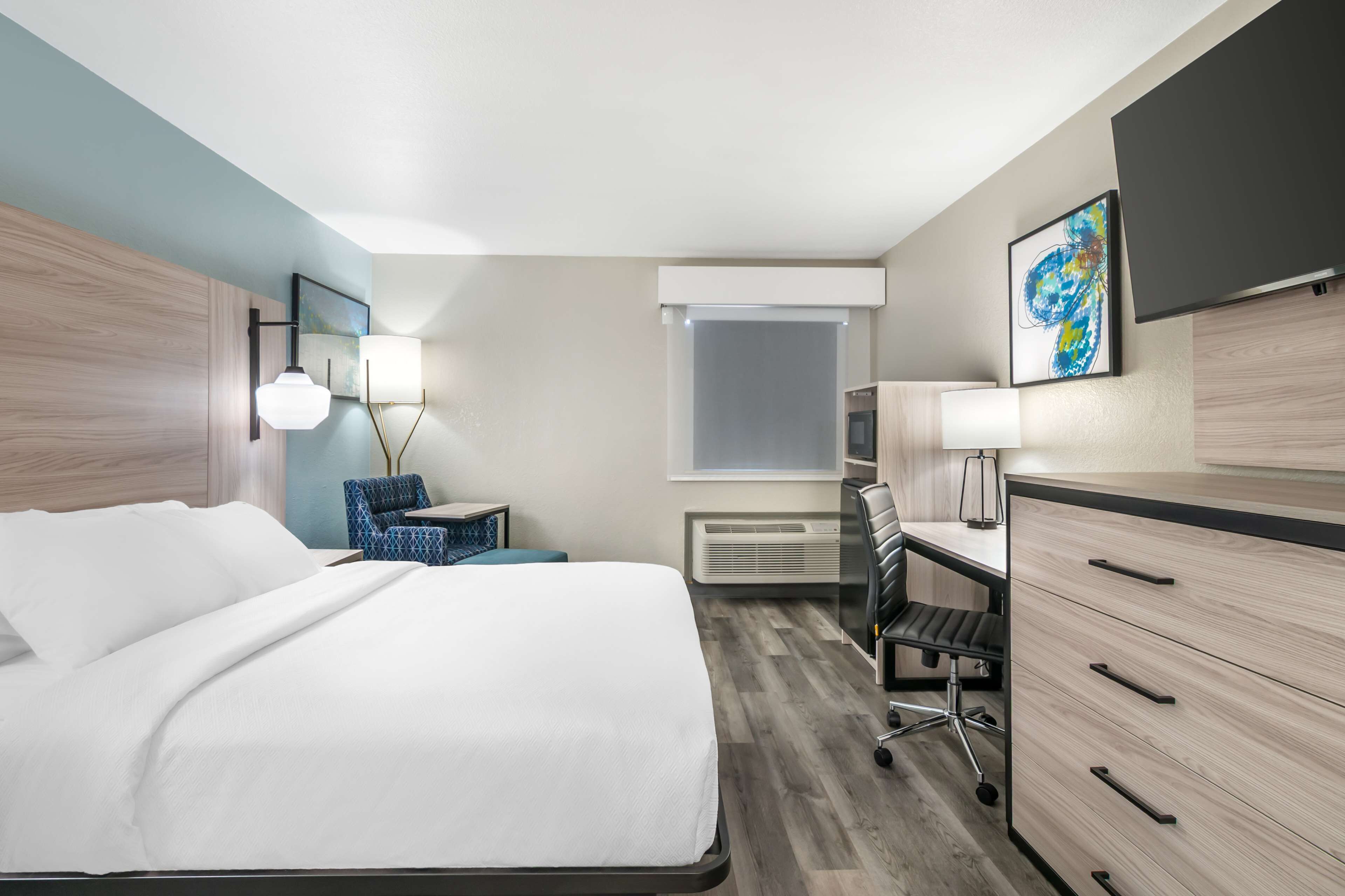 Una habitación de hotel moderna con una cama grande, un escritorio, una silla y un armario.