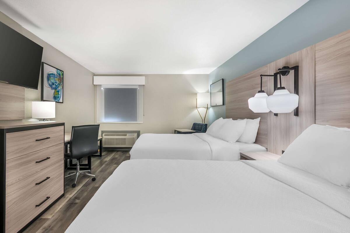 A hotel room with two beds, a desk, a chair, a TV, and a window.