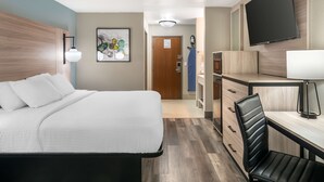 Habitación de hotel con cama, escritorio, silla, televisor y obra de arte en la pared.