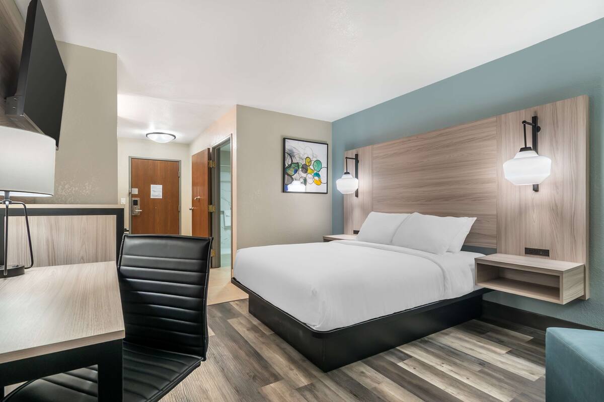 A hotel room with a bed, a desk, a chair, and a wall-mounted light fixture.