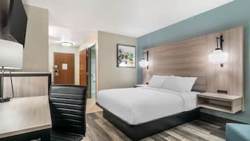 A hotel room with a bed, a desk, a chair, and a wall-mounted light fixture.