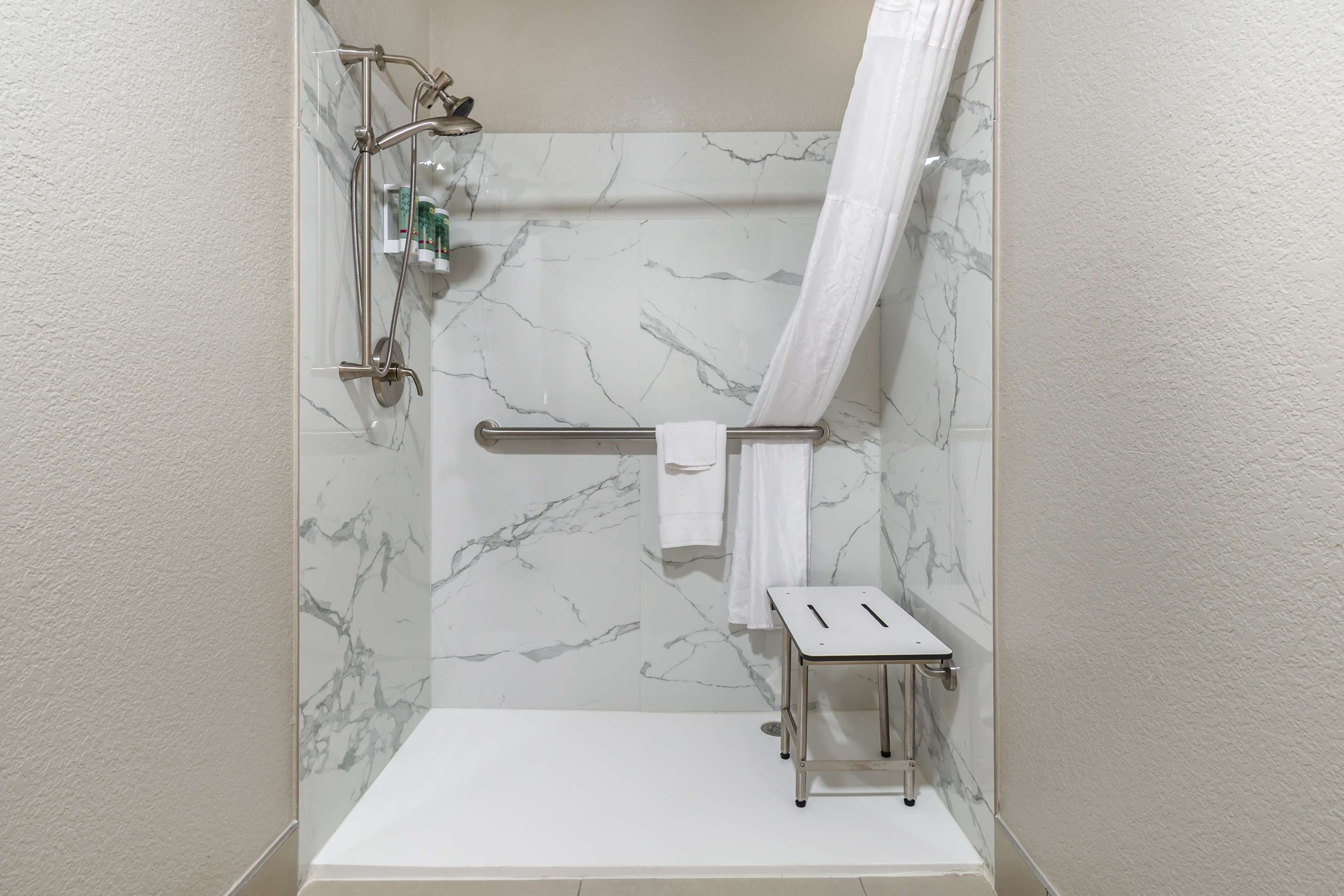 A walk-in shower with a glass door, a handheld showerhead, a handheld showerhead, a towel rack, and a small step stool.