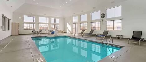 A large indoor swimming pool with clear blue water, surrounded by lounge chairs and a sunbed.