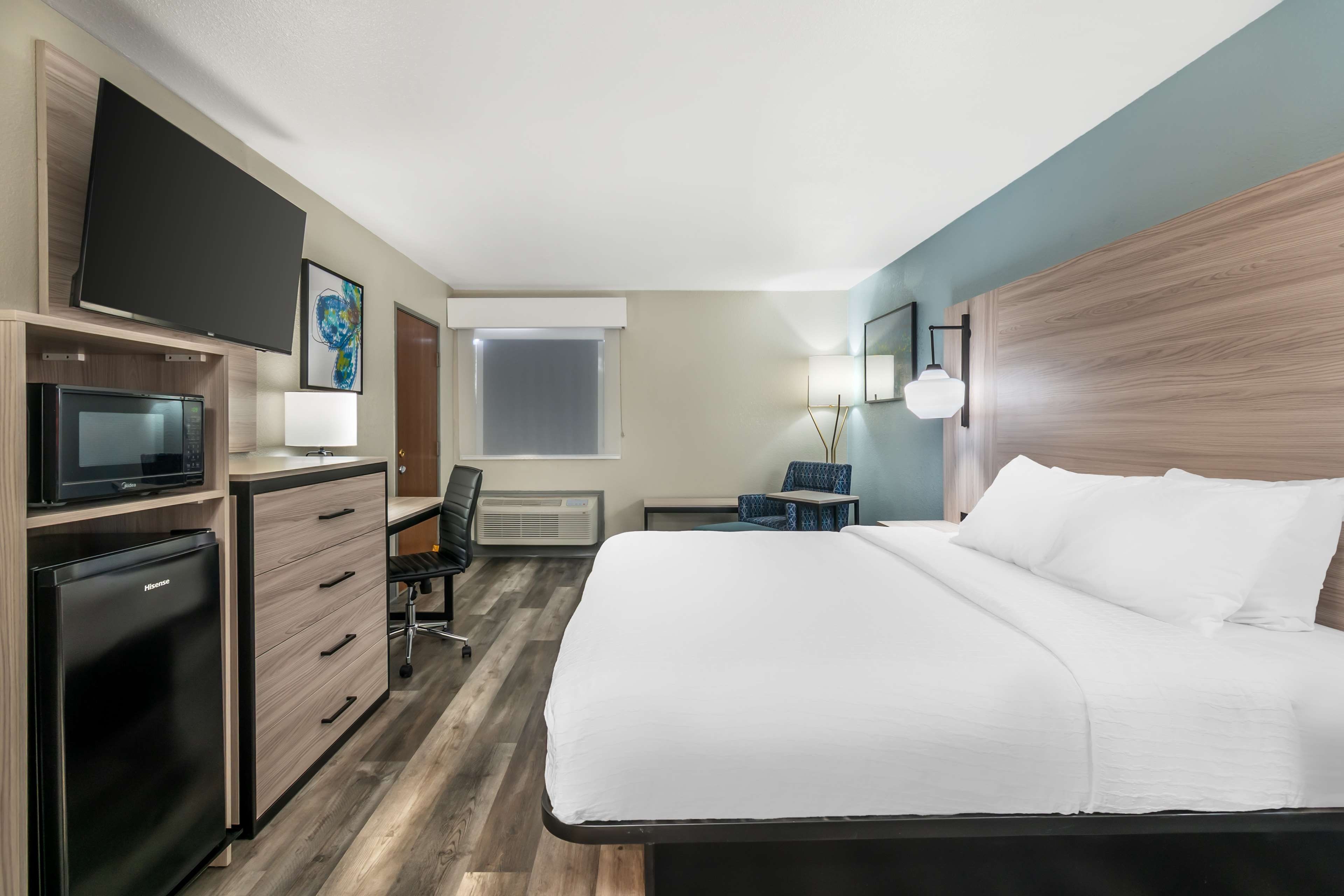 A hotel room with a bed, desk, chair, television, and a flat-screen TV mounted on the wall.