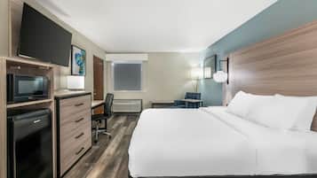 A hotel room with a bed, desk, chair, television, and a flat-screen TV mounted on the wall.