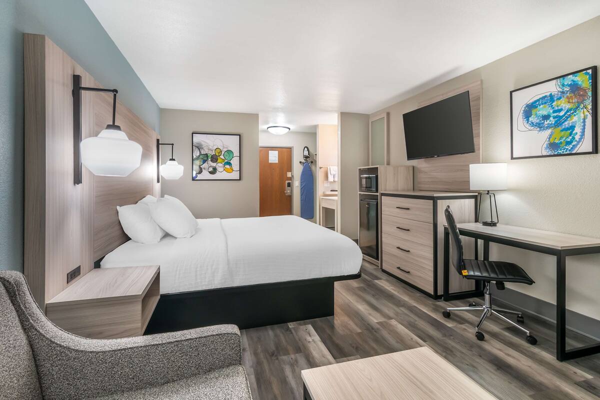 A hotel room with a bed, desk, chair, and a TV on the wall.
