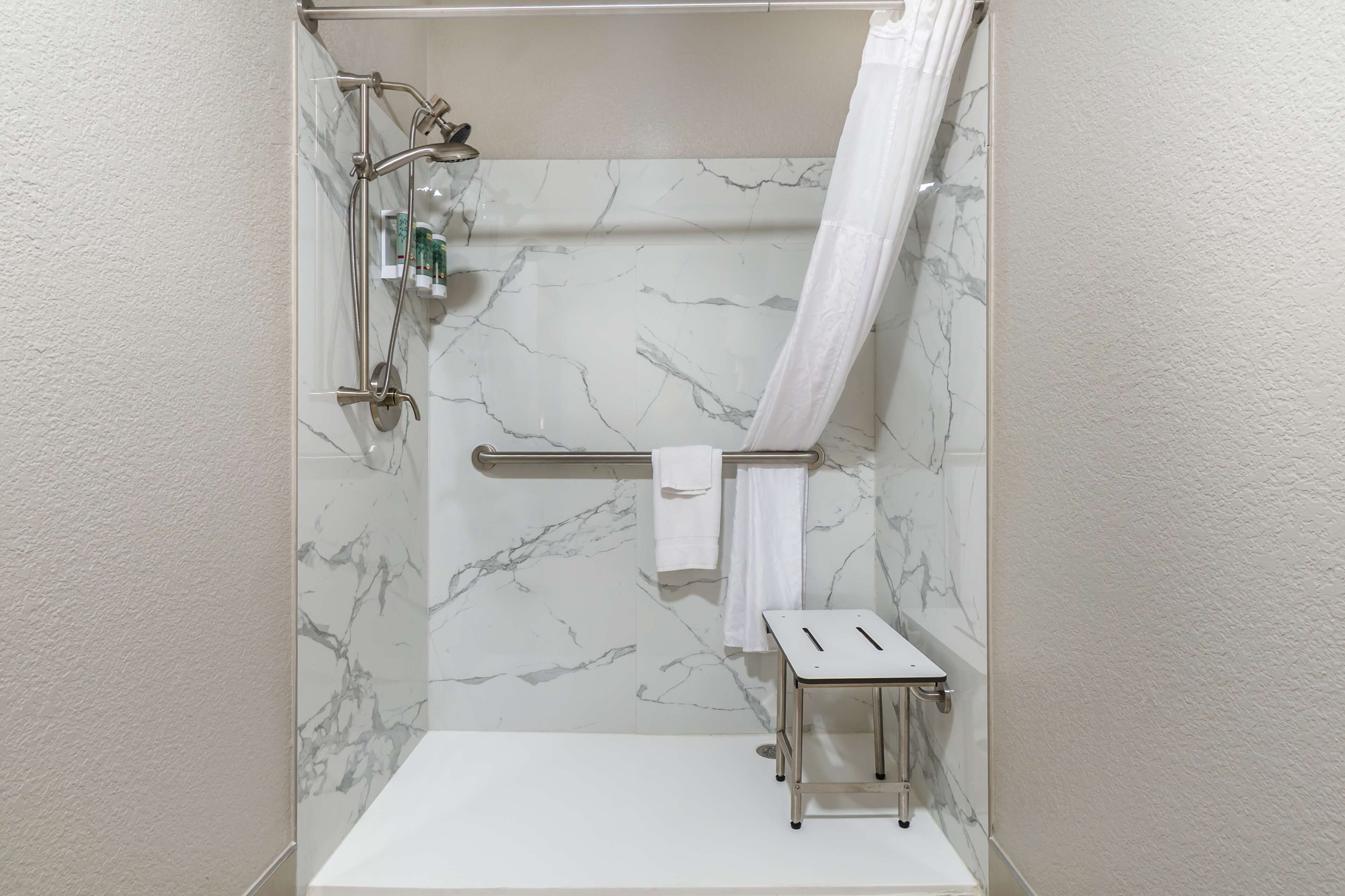 A bathroom with a shower, a towel rack, and a small stool.