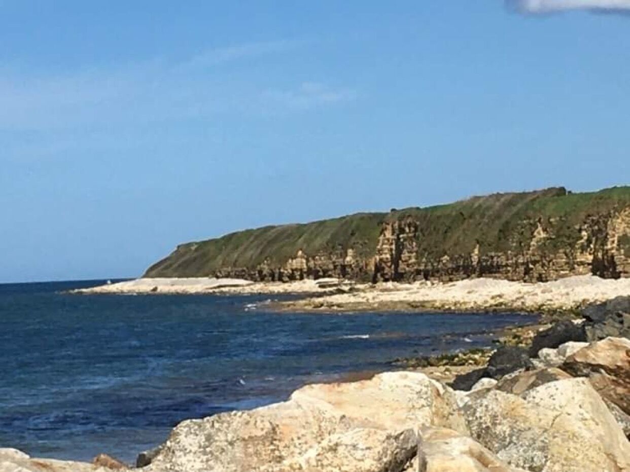 A coastal landscape with rocky terrain and a clear sky.