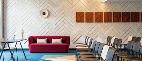 A conference room with a red sofa, rows of chairs, a projector, and a patterned carpet.