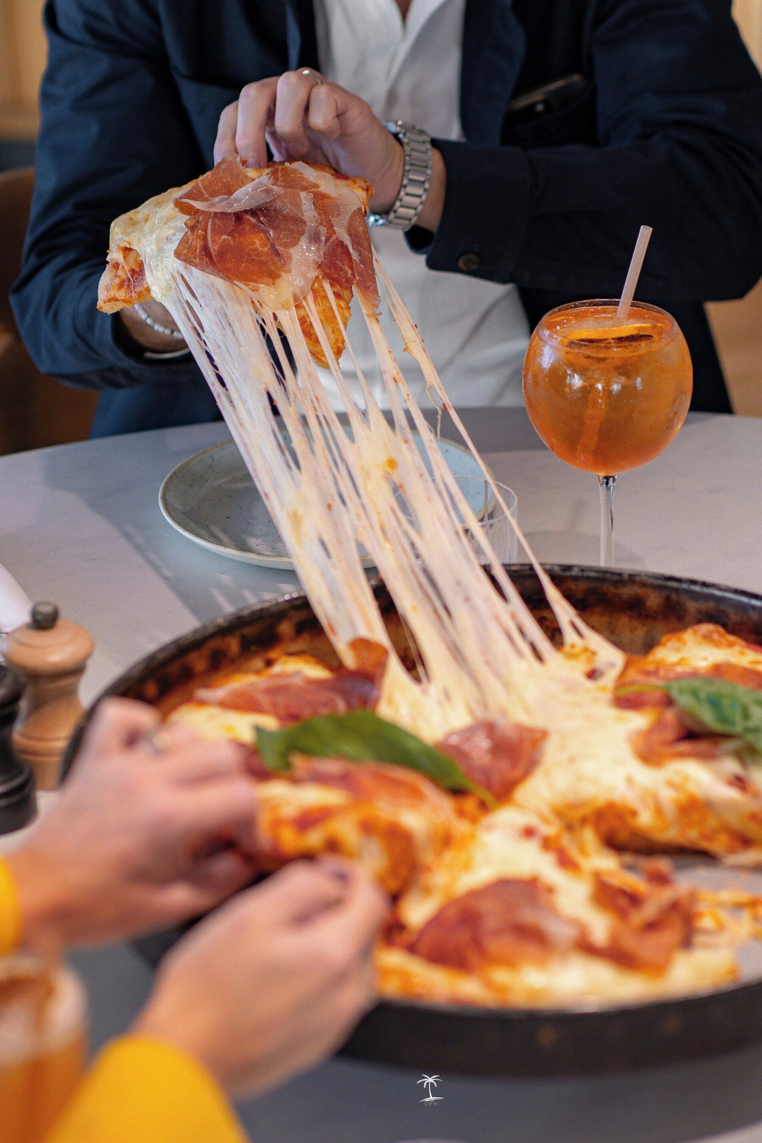 A person pulling a slice of pizza with cheese and pepperoni from a pan.