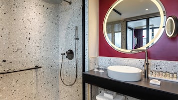 Un baño moderno con una ducha de granito veteado, un espejo redondo y un lavamanos blanco.