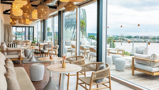 A modern interior with wicker furniture, large windows, and a view of a cityscape. - Renaissance Bordeaux Hotel (Bordeaux)