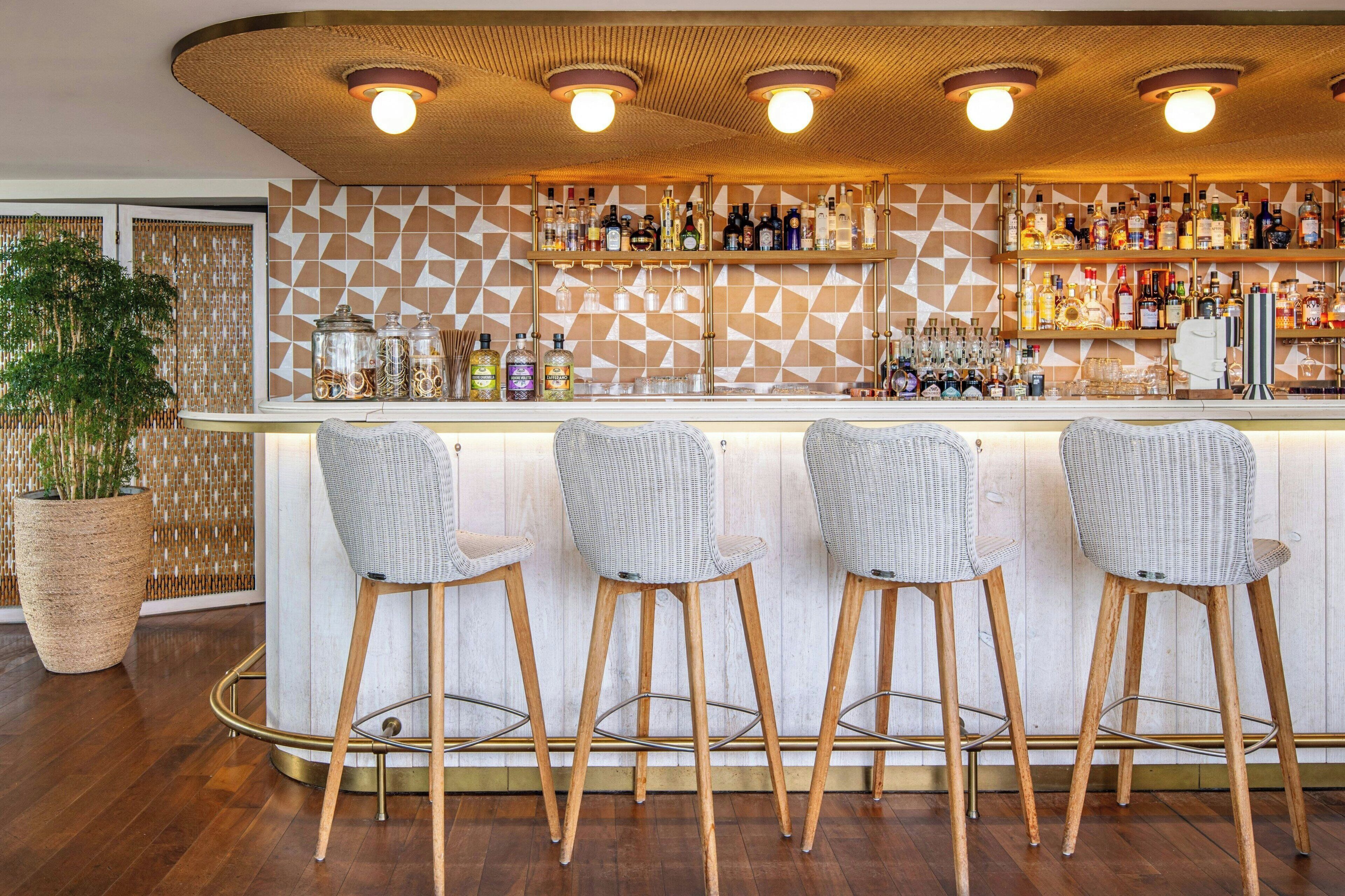 A bar area with a geometric patterned wall, a variety of liquor bottles, and three wicker bar stools.