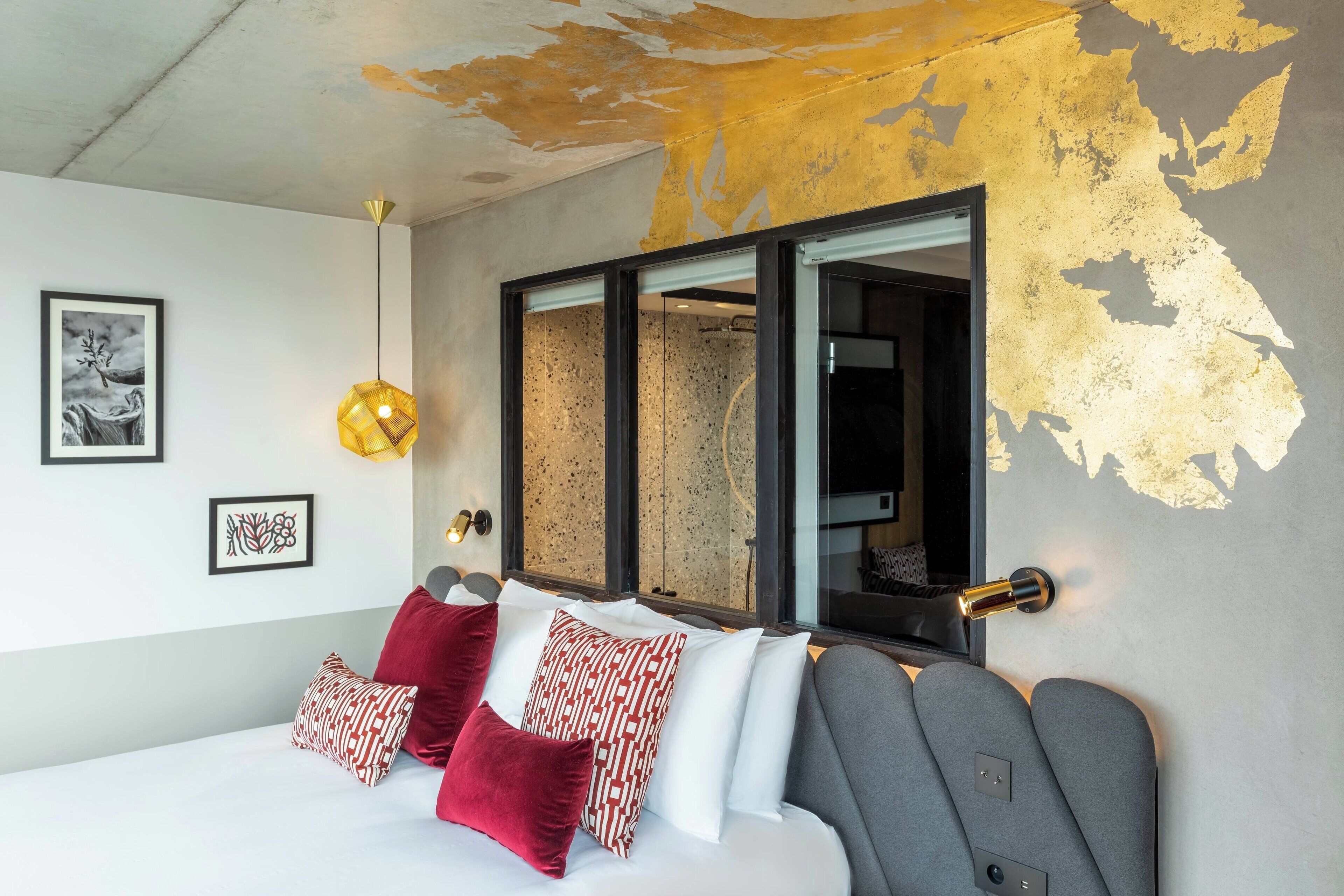 A modern bedroom with a bed, red and white pillows, a framed picture, and a unique wall design.