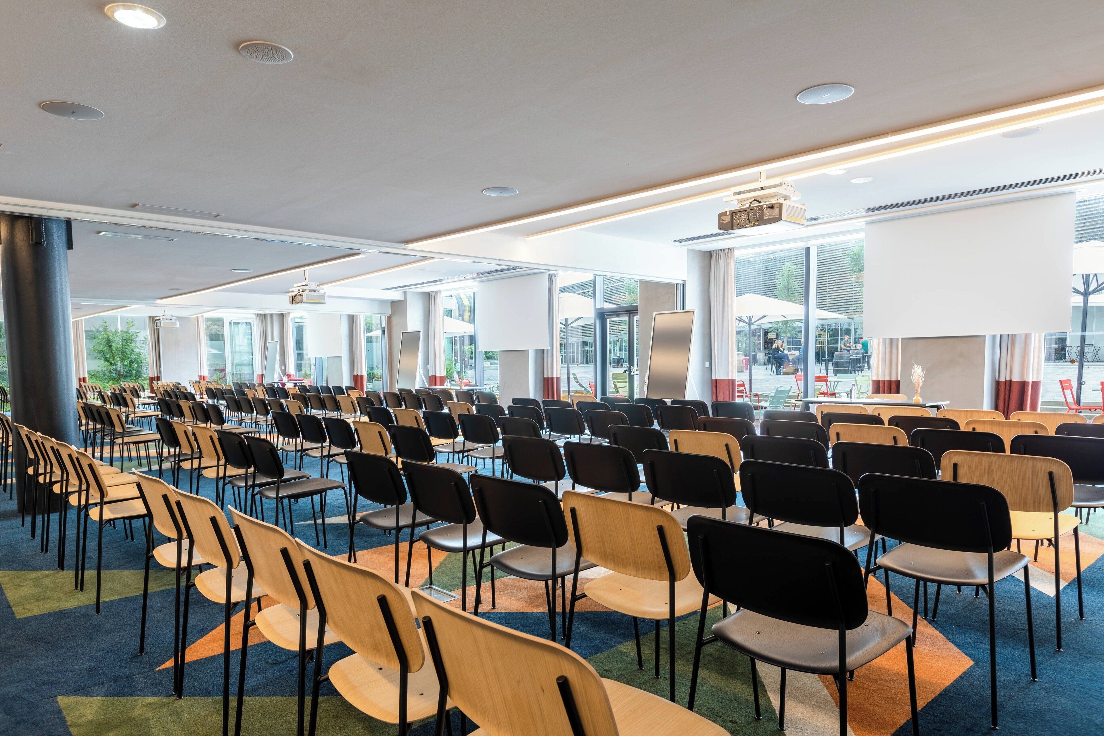 A conference room with rows of chairs and tables, large windows, and a modern ceiling design.