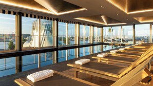 A sunlit room with large windows, a view of a bridge, and multiple sun loungers with towels. - Renaissance Bordeaux Hotel (Bordeaux)