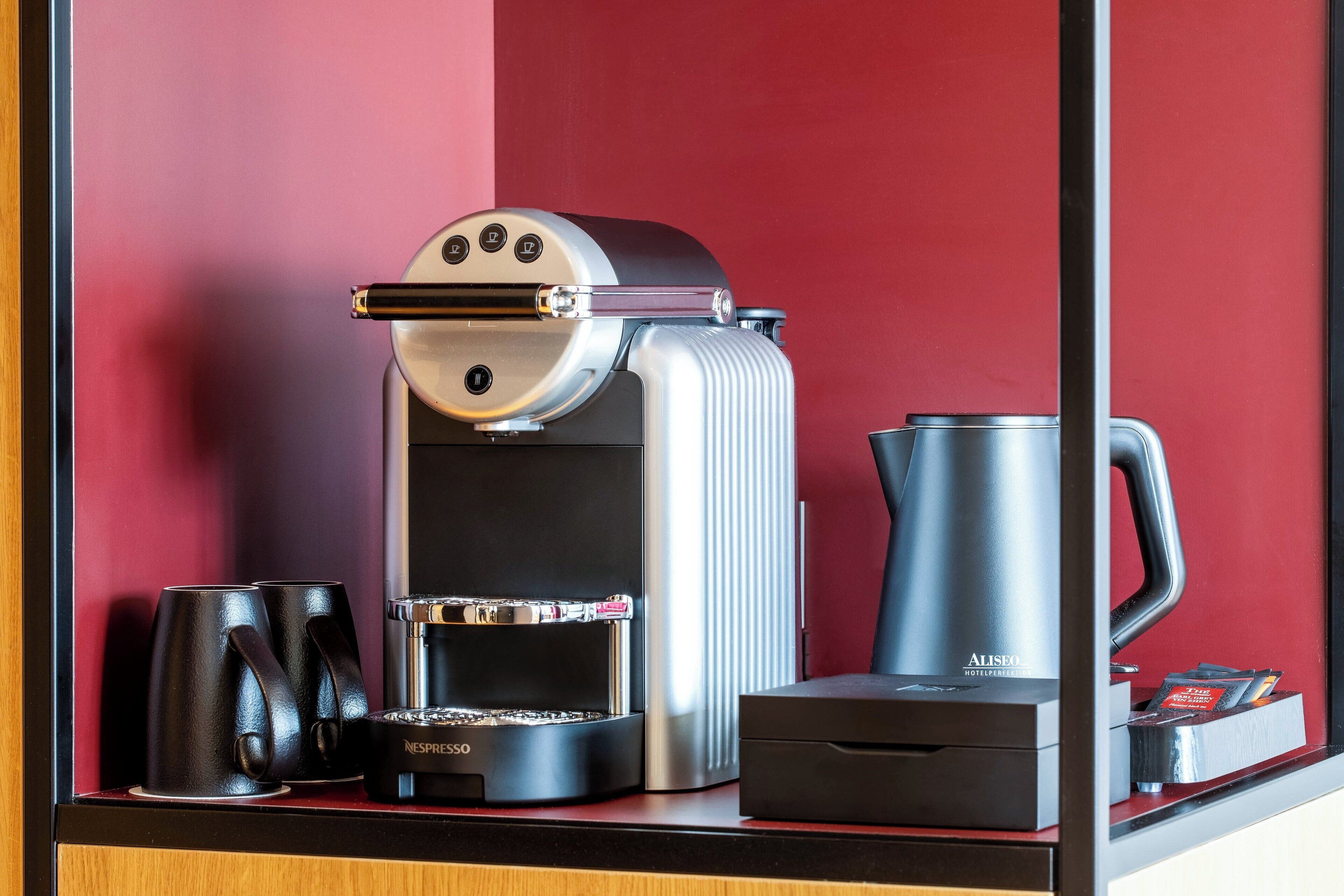 A coffee machine with a Nespresso pod dispenser, a coffee pot, and two cups on a counter.