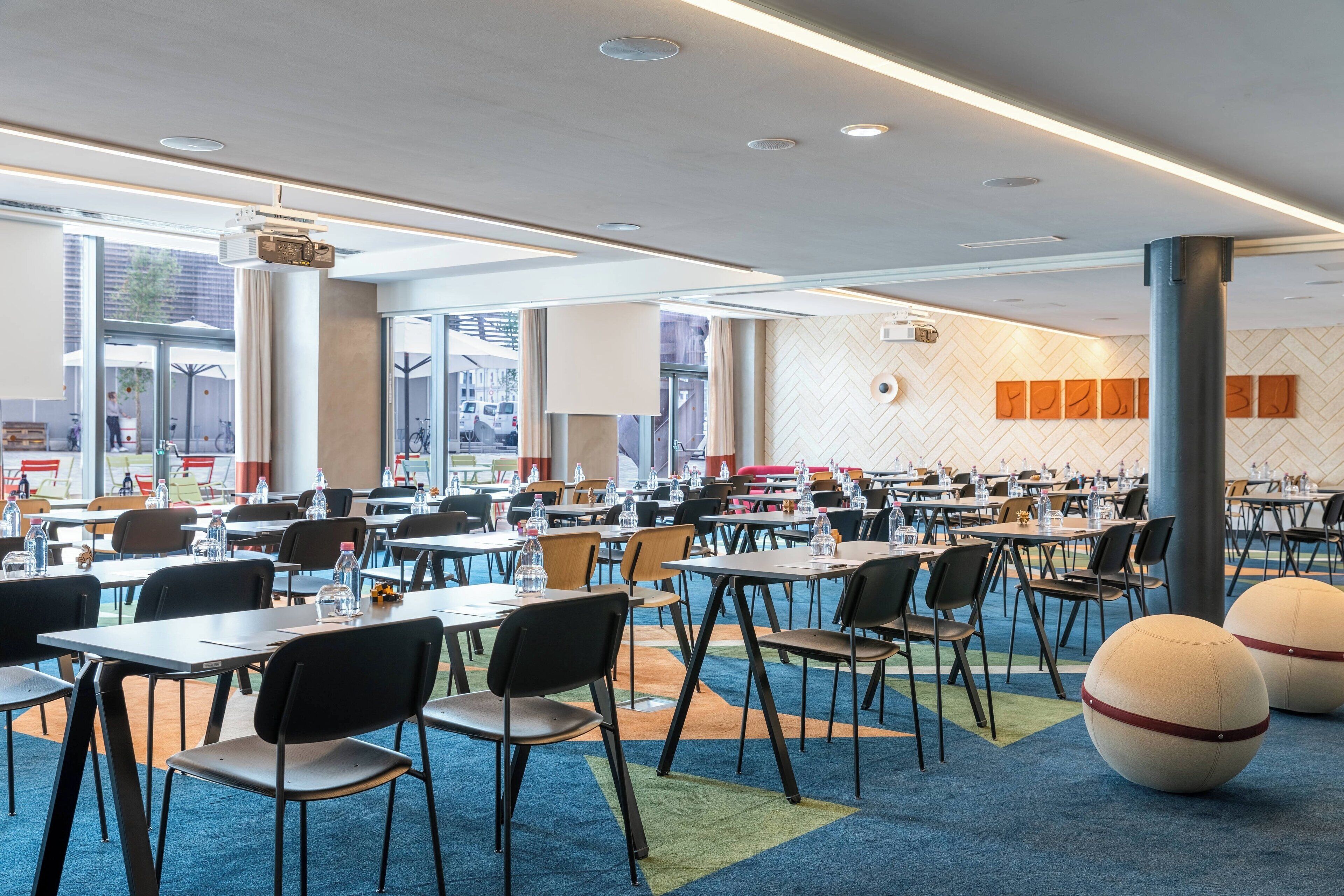 A spacious dining area with multiple tables and chairs, large windows, and a modern ceiling design.
