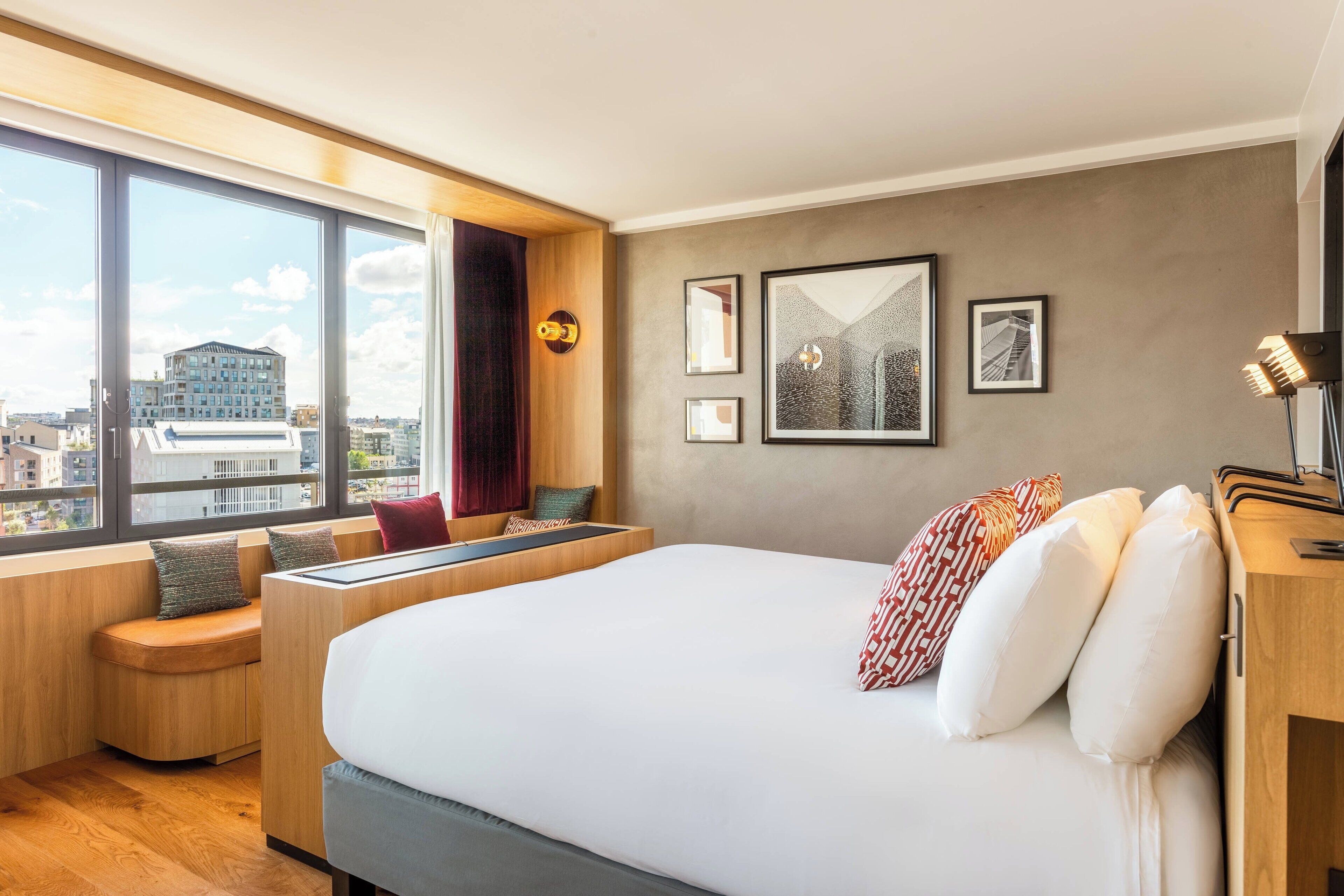 A modern hotel room with a large bed, a seating area, and large windows offering a city view.