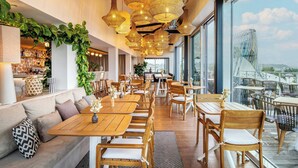 A restaurant with wooden tables and chairs, hanging wicker chandeliers, and a view of a bridge. - Renaissance Bordeaux Hotel (Bordeaux)