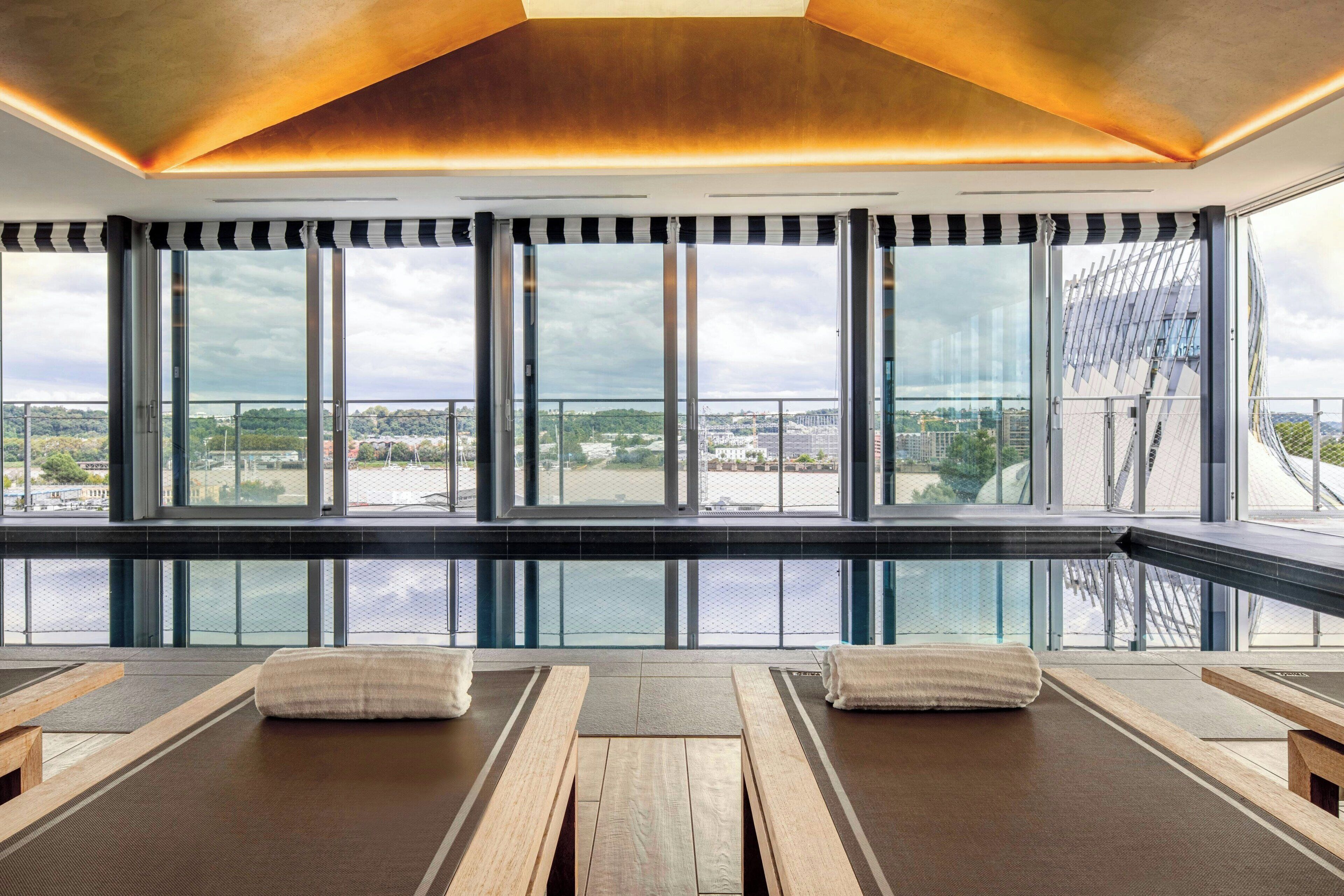 A modern spa area with large windows, wooden loungers, and a view of the city.