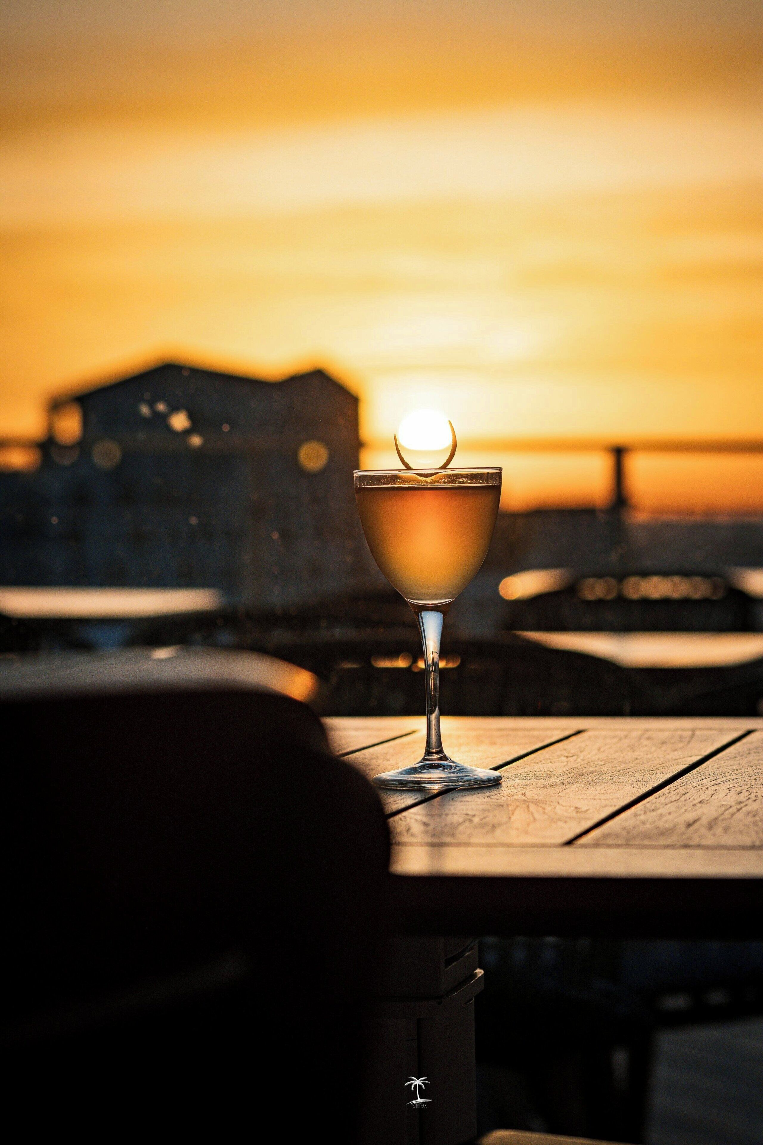 A cocktail glass on a wooden table with a sunset in the background.