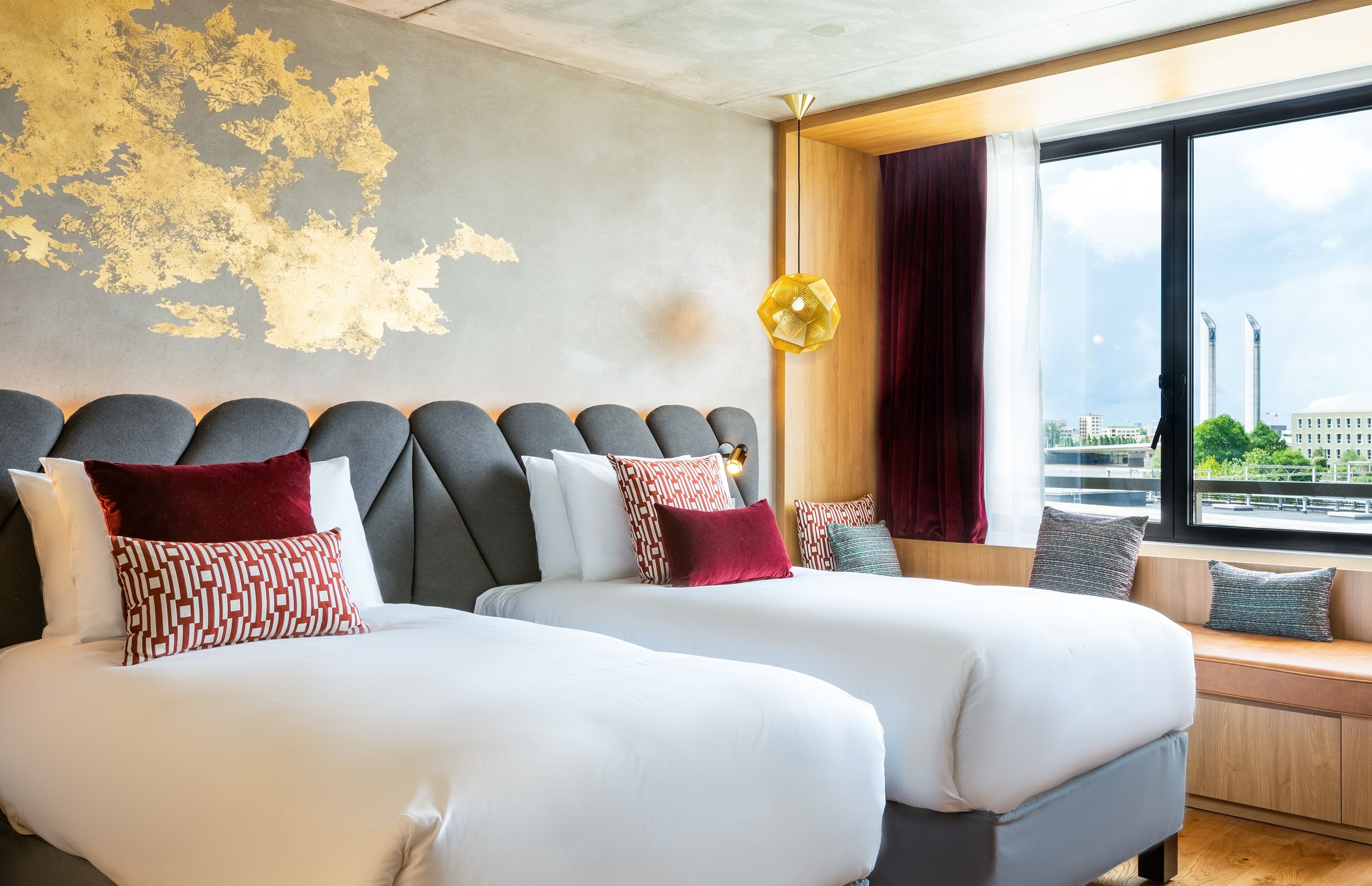 A hotel room with two beds, a large window with a city view, and a unique wall design.