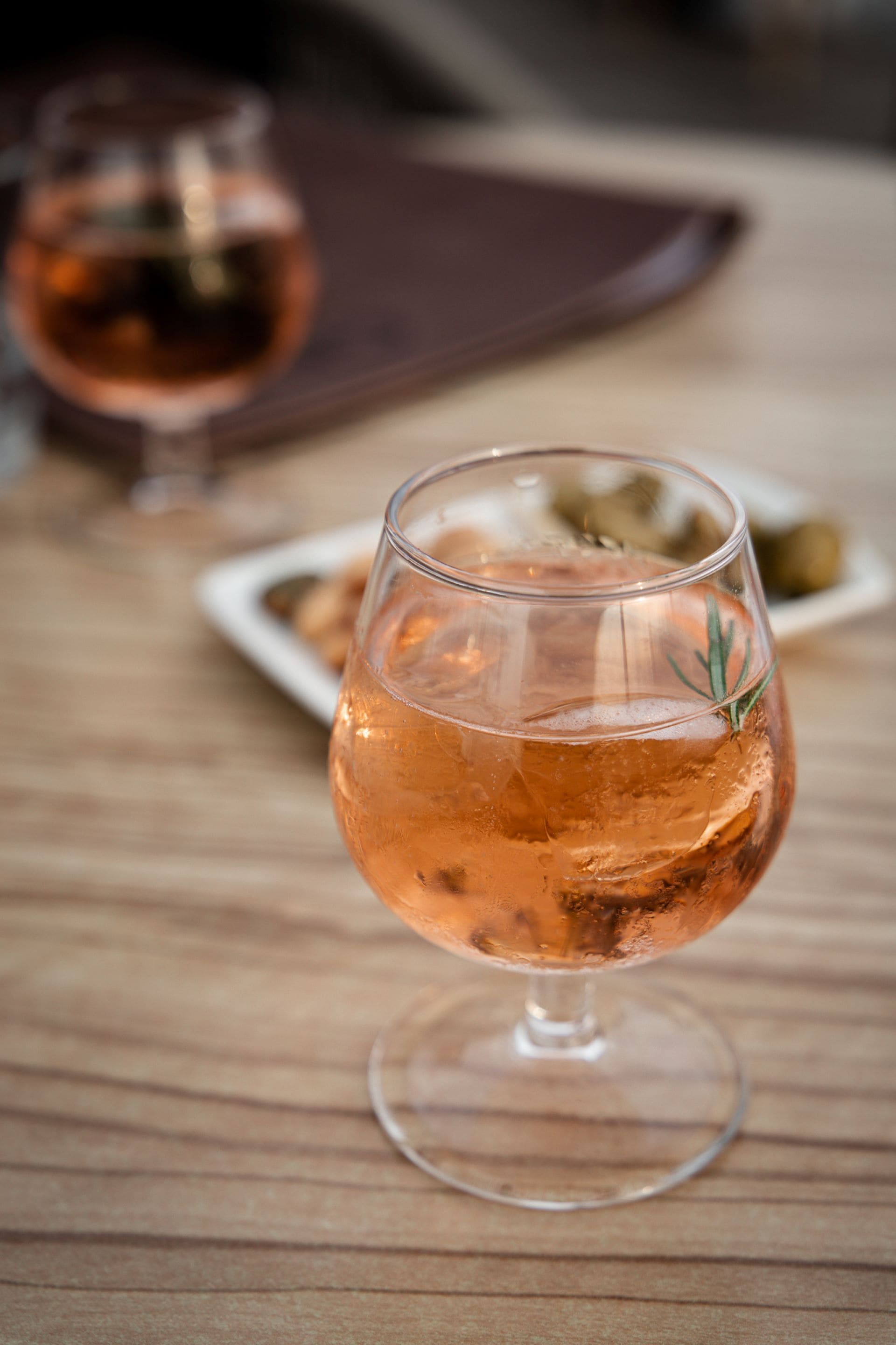 A glass of rosé wine with a rosemary sprig on a wooden table.