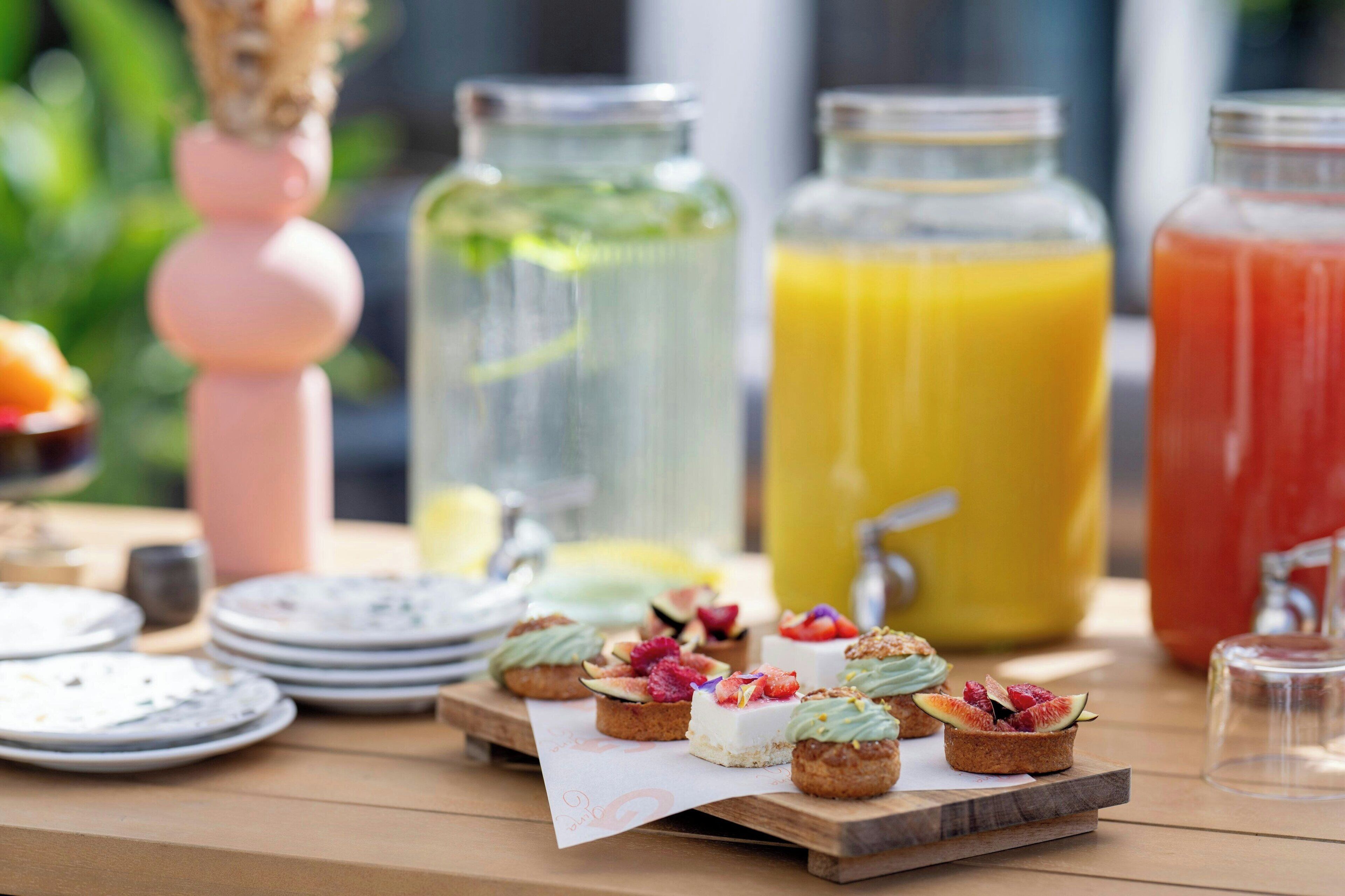 Een tafel met diverse etenswaren en dranken, waaronder fruit taartjes en verschillende soorten sap.