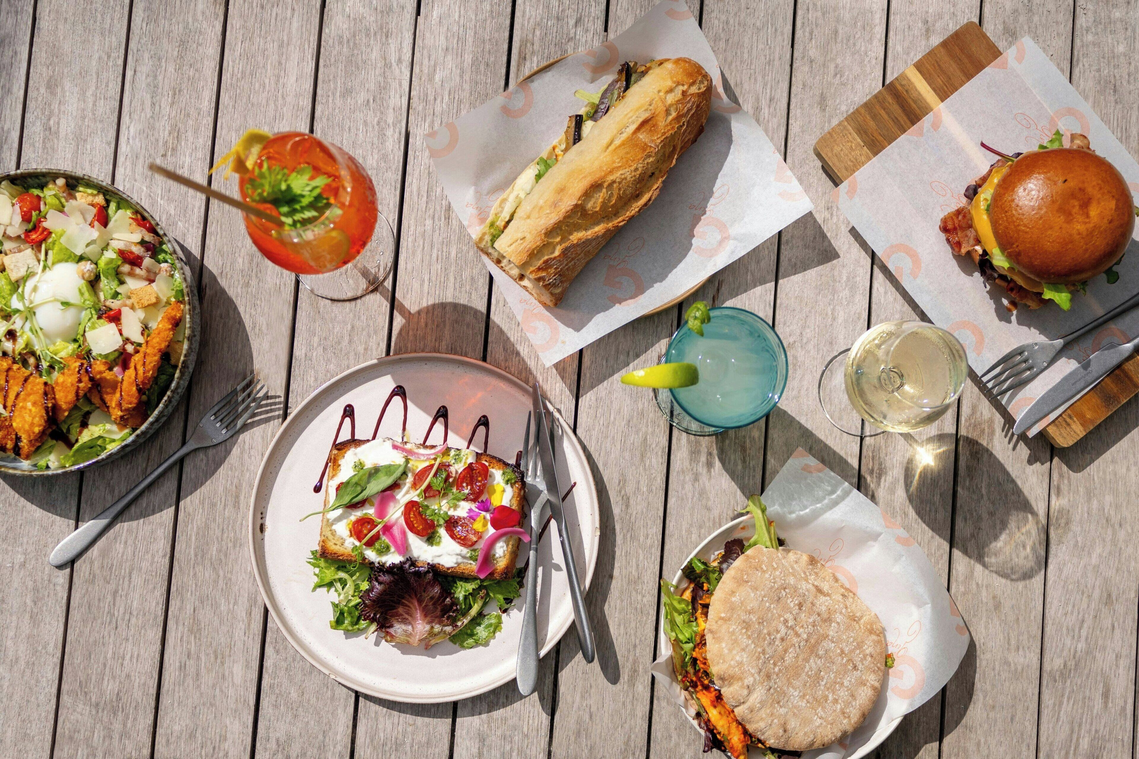 Una mesa de madera con varios platos, incluyendo una ensalada, sándwiches y una bebida.