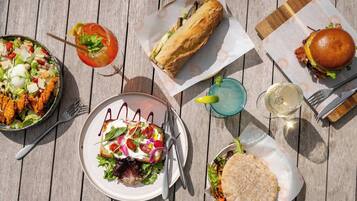Una mesa de madera con varios platos, incluyendo una ensalada, sándwiches y una bebida.