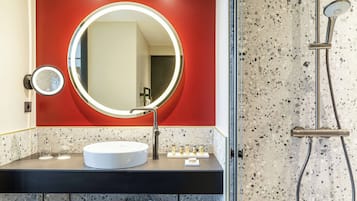 Un baño con espejo redondo, lavabo y ducha.