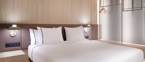 A modern hotel room with a large bed, two bedside tables with lamps, a wooden headboard, and a large window with a view.