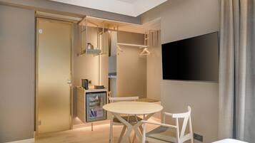 Una habitación de hotel moderna con una mesa de comedor de madera, sillas blancas, un televisor de pantalla plana y un mini bar.