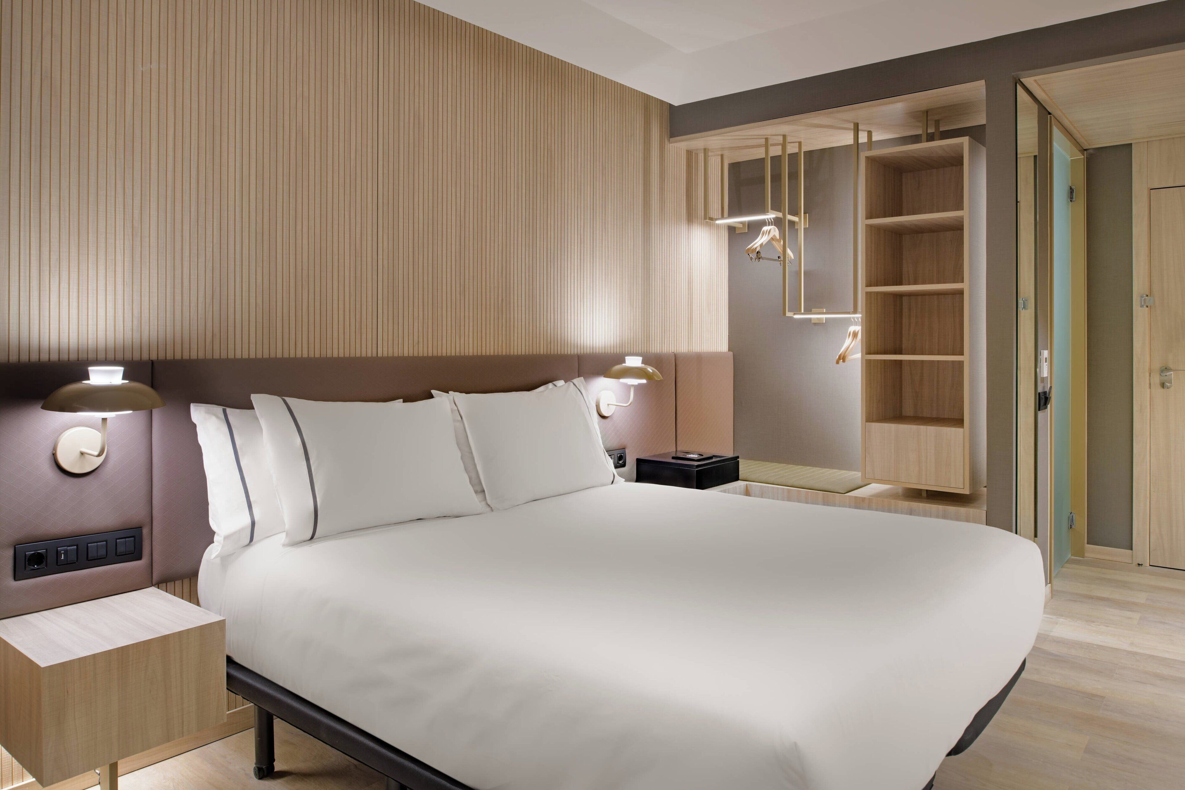Habitación de hotel moderna con una cama grande, lámparas de noche, una mesita de noche y un armario empotrado con espejo.