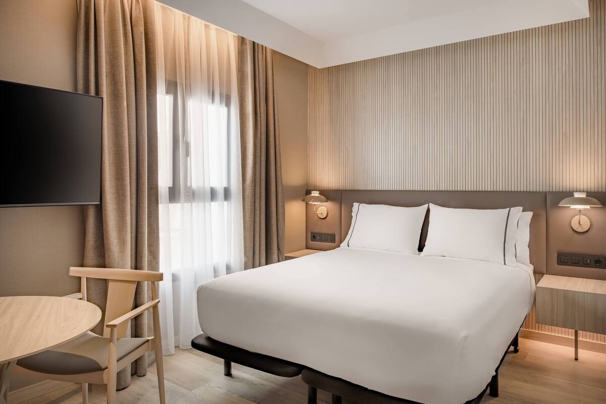 Ein Hotelzimmer mit einem großen Bett, einem Fernseher, einem Schreibtisch und einem Sessel.