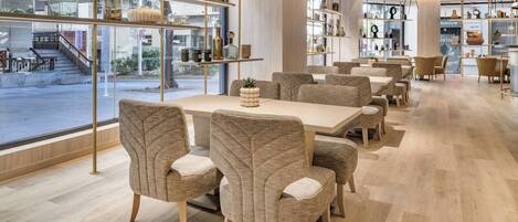 Un espace repas moderne, avec une longue table et des chaises rembourrées, entouré d’étagères où sont exposés des objets décoratifs.
