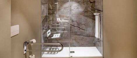 A modern bathroom with a glass-enclosed shower, marble walls, and a white sink.