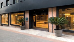 Een moderne hotelentree met grote glasramen, een receptiebalie en twee potplanten.