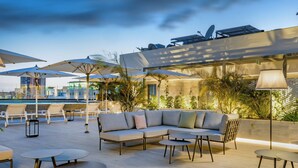 Een terras met een bank, ronde tafels en parasols.